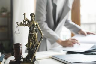 Person looking through papers with a statue of Lady Justice on the desk.