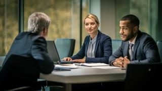 Three people sitting at a table and talking during a business meeting.