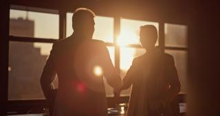 two silhouettes of people shaking hands in an office  