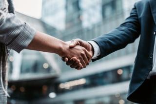 Two business persons shaking hands standing outside office building