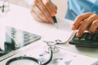 person with a stethoscope writing on papers with a calculator next to hand