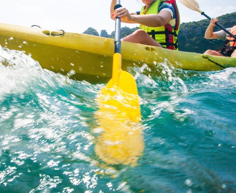 Close shot of explorer women in life jackets paddling the kayak with splashes
