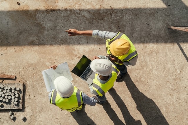 Workers using computer and blueprint at construction site