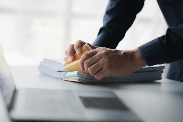 Businessman sorting stacks of department meeting papers, document management in corporate office.