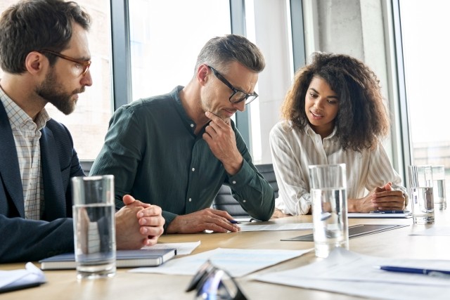 Focused mature businessman reading contract considering risks with lawyers