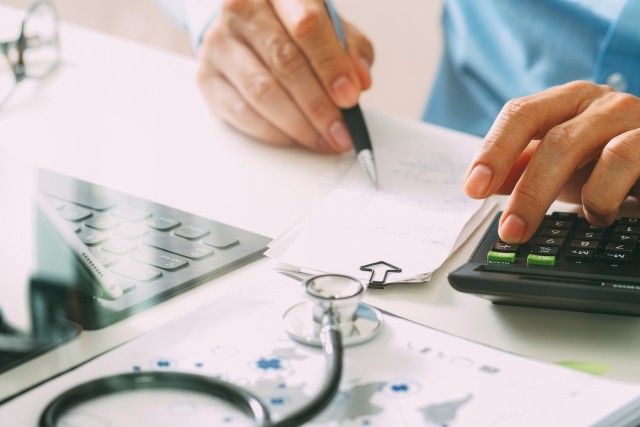person with a stethoscope writing on papers with a calculator next to hand