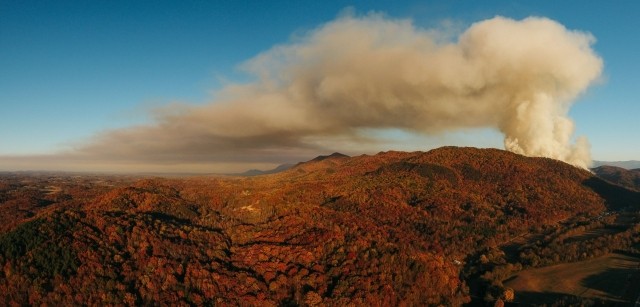A canyon in Fall colors under a vast blue sky with a column of smoke rising into it stock photo used by Woodruff Sawyer.