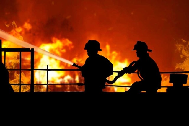 Silouette of two firefighters hosing fire flames