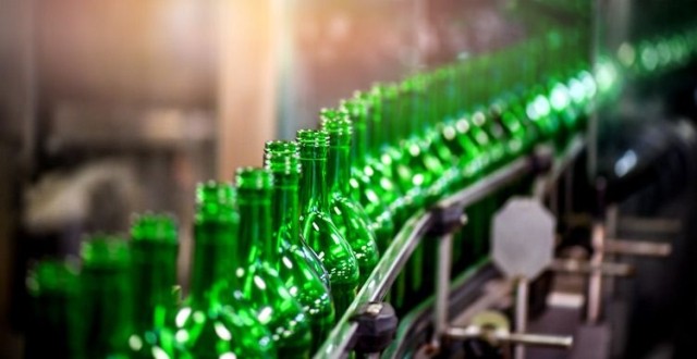 Green glass bottles on conveyor belt of manufacturing facility.