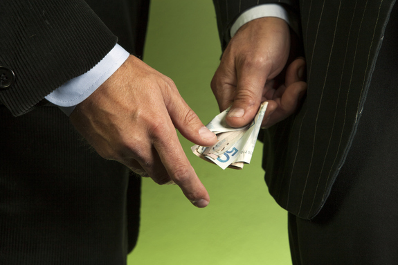 An image of a businessman handing dollars to another businessman outside.
