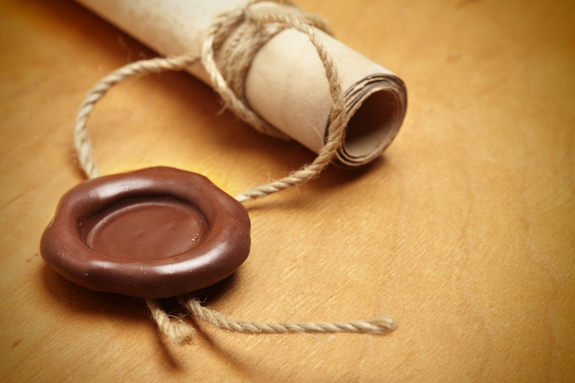 An image of an old document wrapped in a small rope and brow wax seal on a brown table.