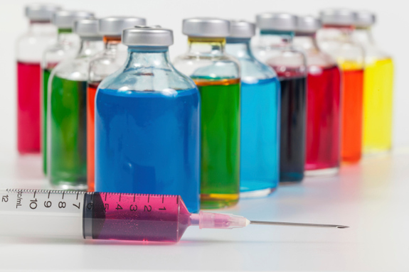 An image of a syringe filled with liquid and a bottles of colorful liquid on a table.