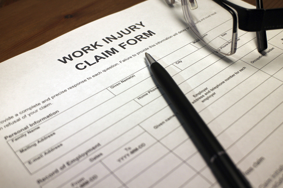 An image of a work injury claim form on a brown table, with glasses, and a pen.