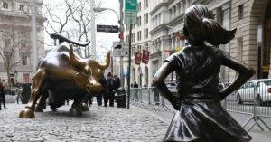 An image of a fearless girl statue facing the Wall St. bull statue.